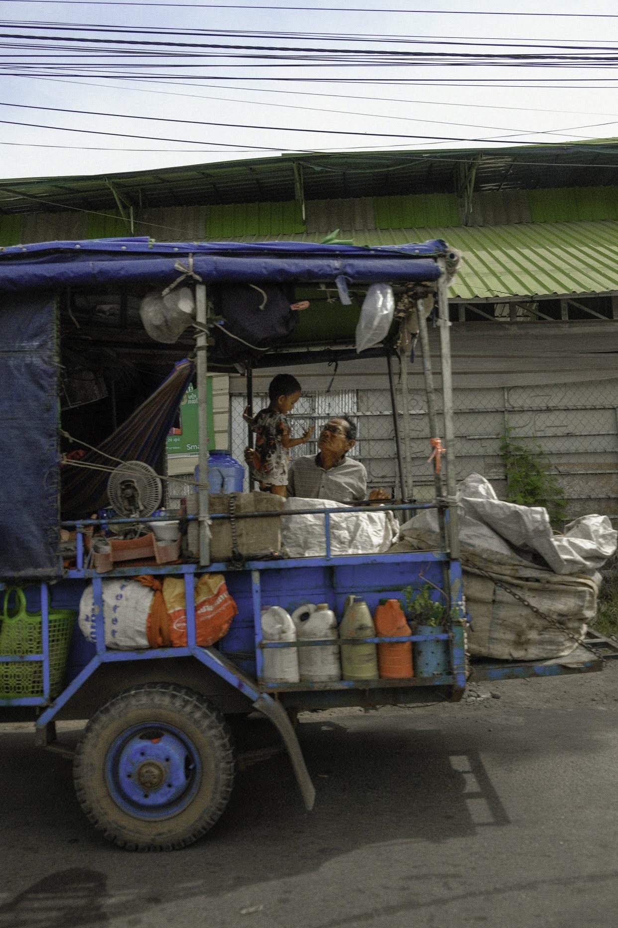 A loaded truck on a roadside, a man and a small boy under its canopy.